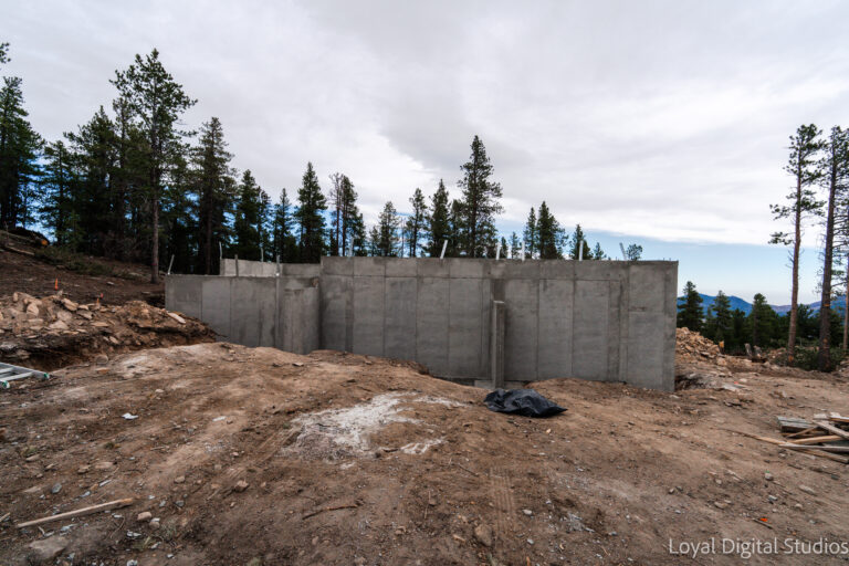 Poured concrete foundation walls on a mountain construction site in Colorado with excavation and forest surroundings.