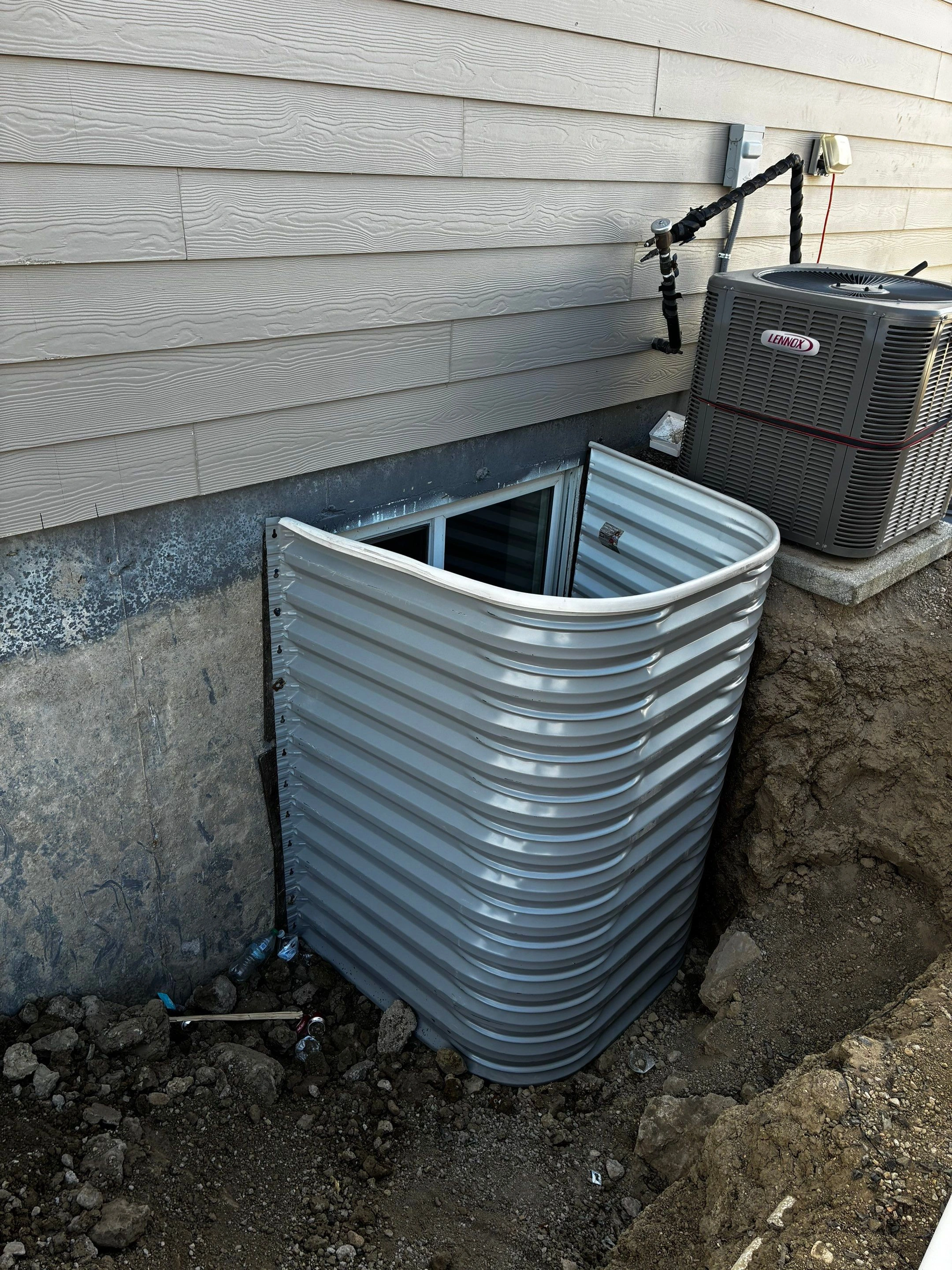 New basement egress window and corrugated metal window well installed beside a foundation during Fort August Foundation work in Berthoud