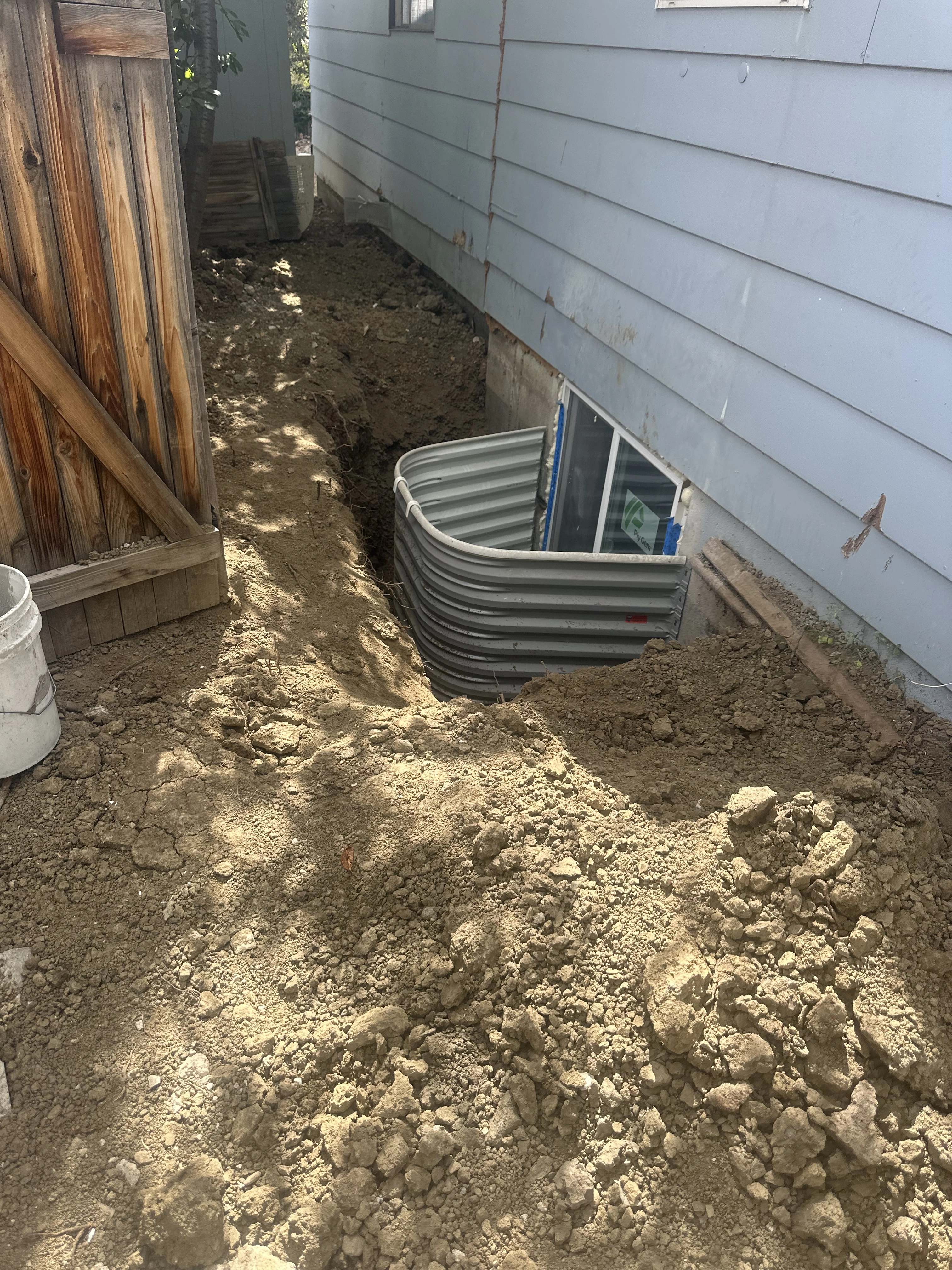 Basement egress window and corrugated metal window well beside excavation during installation in Longmont by Fort August Foundation