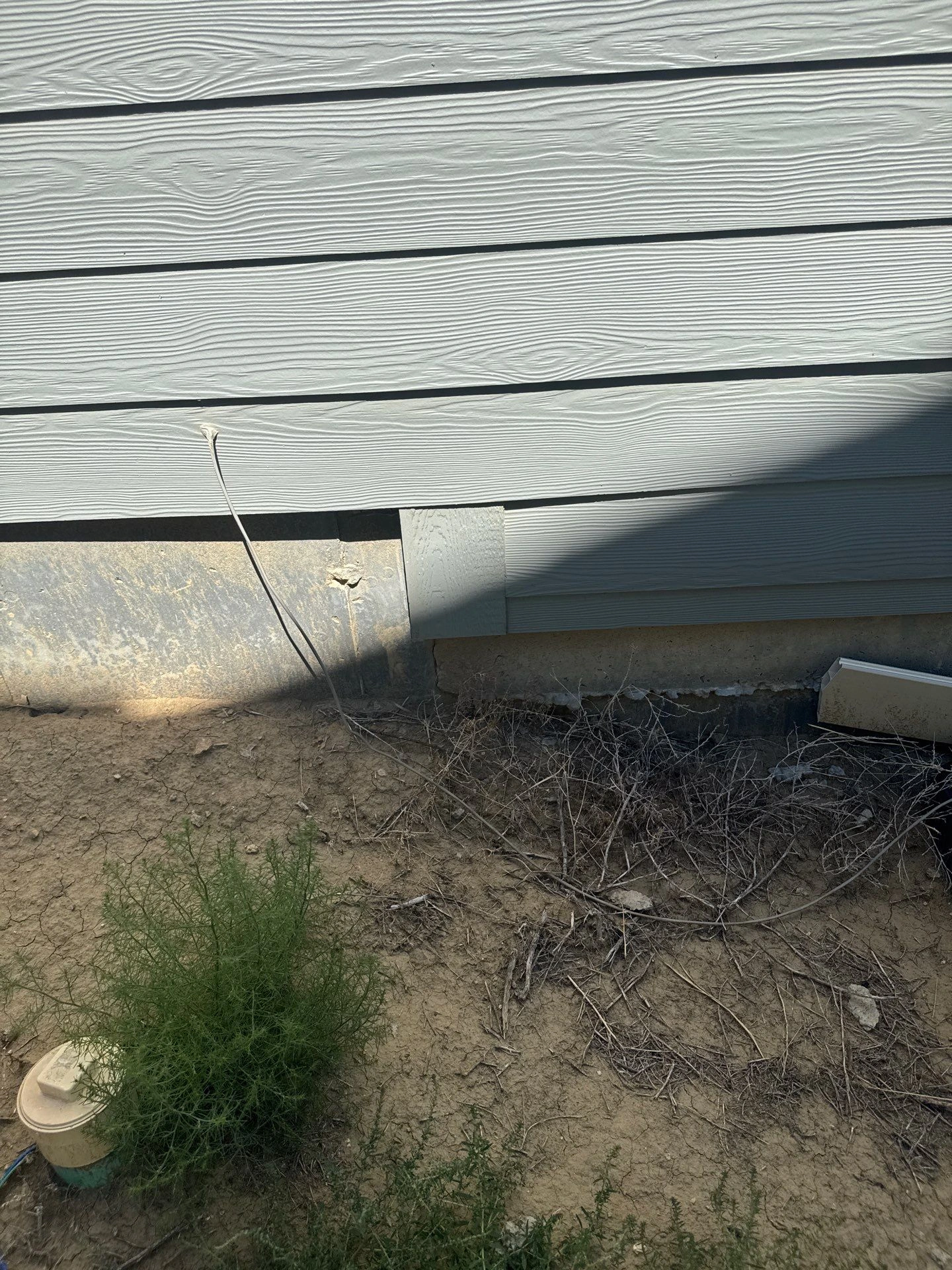 Visible cracking along an exposed exterior concrete foundation beneath siding during a foundation inspection in Colorado Springs by Fort August Foundation