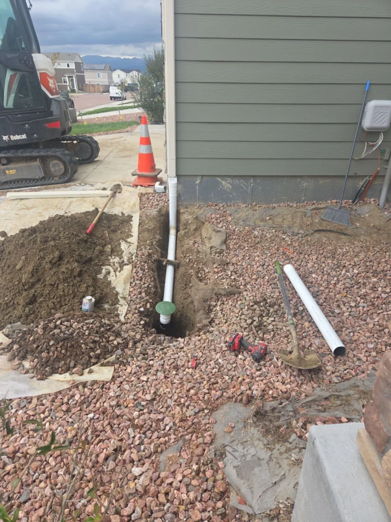 PVC drainage pipe and cleanout in an excavated trench beside a home during foundation repair in Colorado Springs by Fort August Foundation