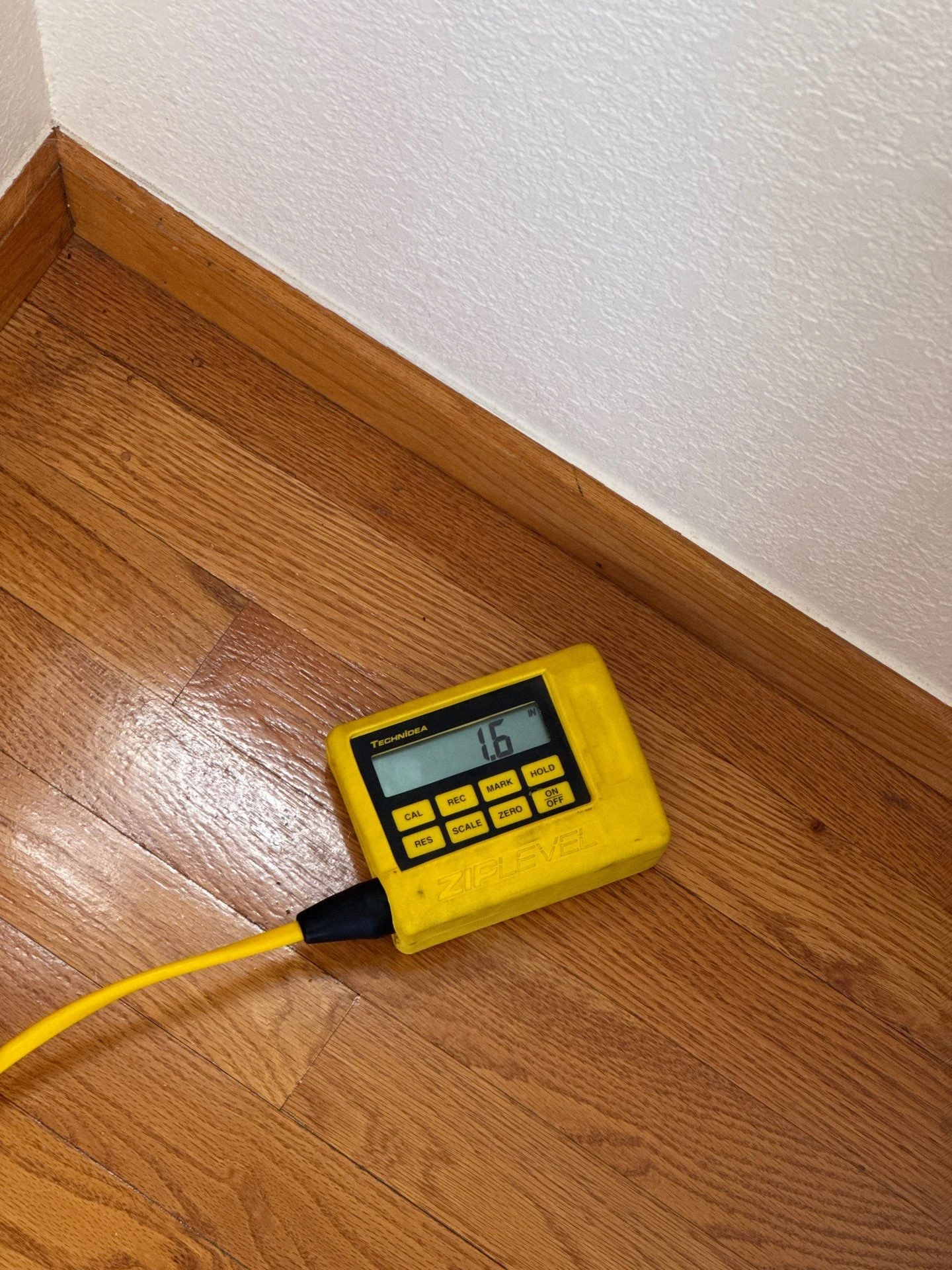 Yellow ZipLevel digital level on hardwood floor during a foundation inspection in Louisville by Fort August Foundation
